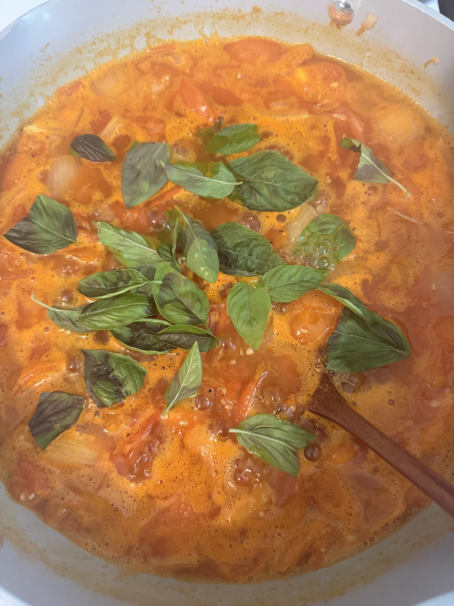 A pot of tomato sauce simmering with fresh basil leaves on top