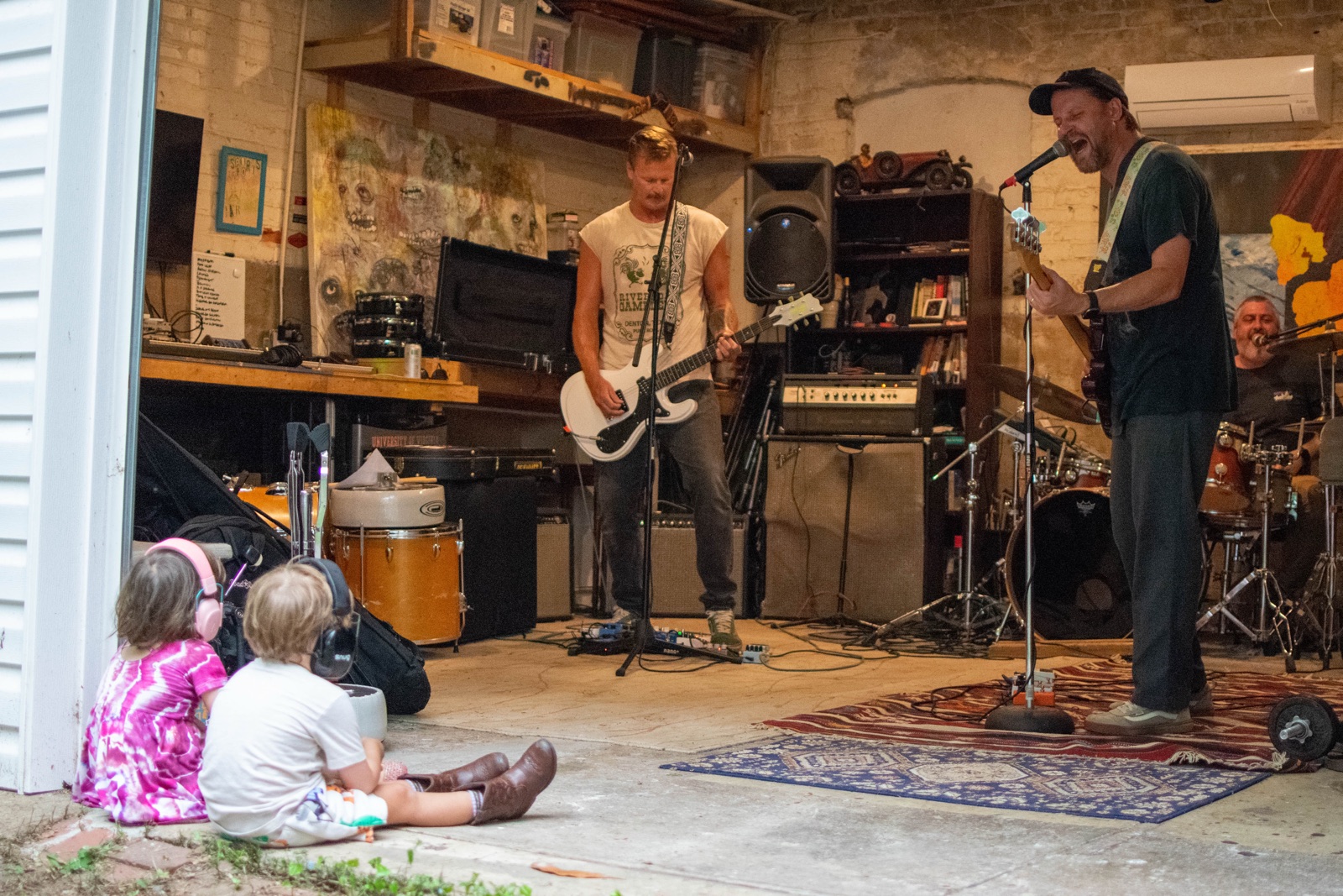 The band playing in an open garage while two young children watch from the driveway
